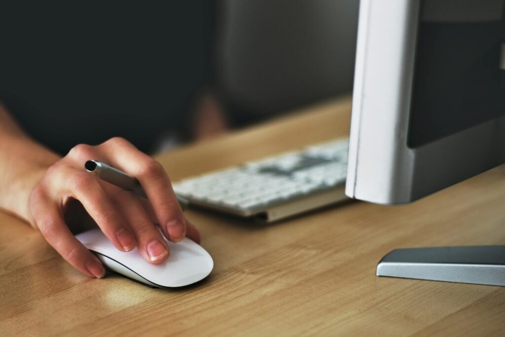 A person's hand gracefully operates a sleek computer mouse on a polished wooden desk, indicative of a modern home office setting suitable for telecommuting or managing real estate listings online, and people keep in touch with him to get an offer in future