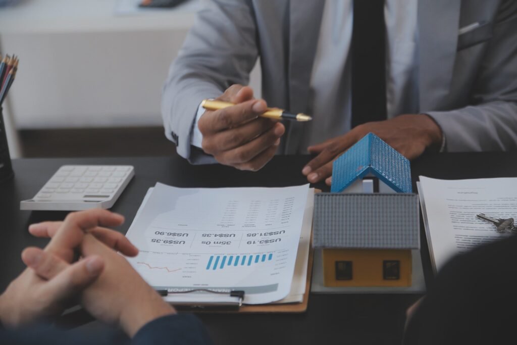 Professional real estate agent presenting financial graphs and investment reports during a consultation with a client, with a model house and keys on the table indicating property overview and investment opportunities.